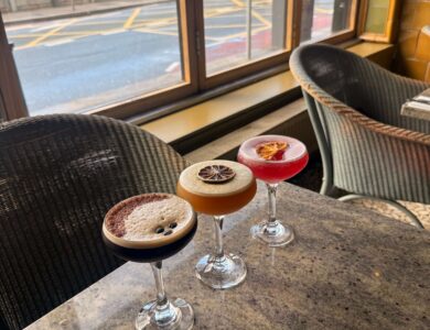 Three elegant cocktails by a window in a cosy Dublin hotel setting.