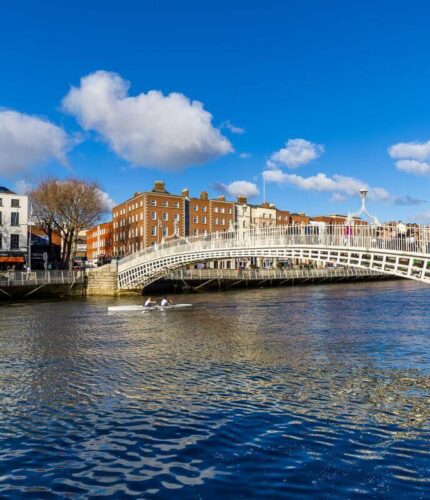 Ha'penny Bridge over the River Liffey in Dublin, with rowers and historic buildings nearby.