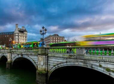Bustling Dublin city bridge with buses and historic buildings at dusk.