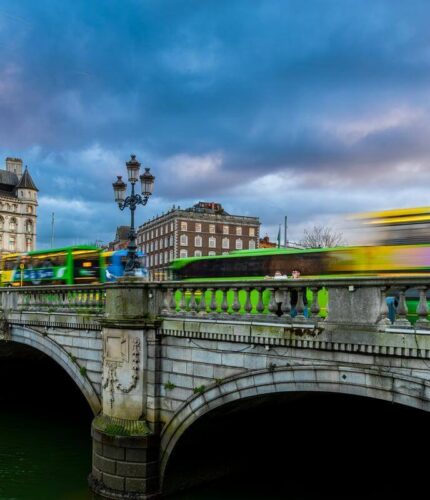 Bustling Dublin city bridge with buses and historic buildings at dusk.