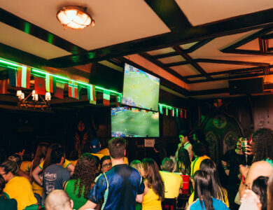Guests watching sports in a lively hotel bar with flags and large screen.