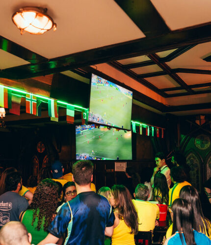 Guests watching sports in a lively hotel bar with flags and large screen.