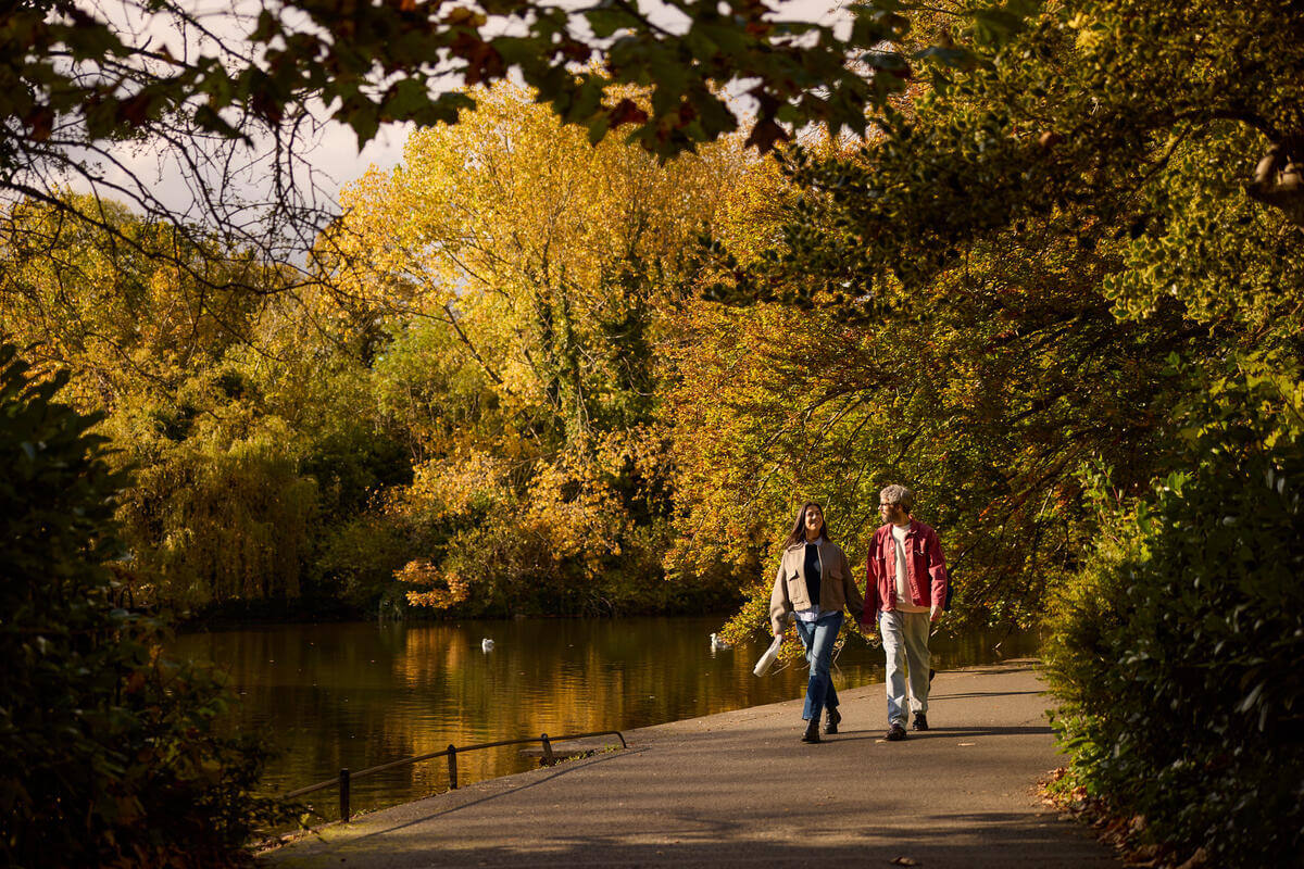 Two people strolling by a serene autumn lake, surrounded by vibrant foliage.