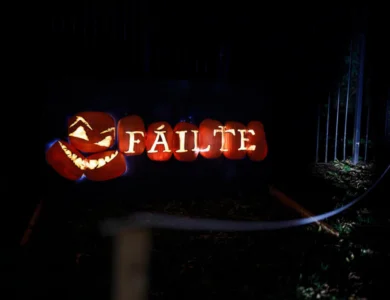 Illuminated carved pumpkins spelling "FÁILTE" with a grinning jack-o'-lantern welcome sign at night