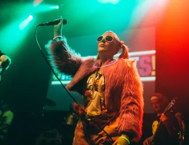 Colourful performer sings energetically on stage in vibrant club setting.