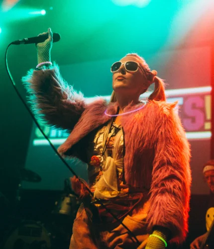 Colourful performer sings energetically on stage in vibrant club setting.